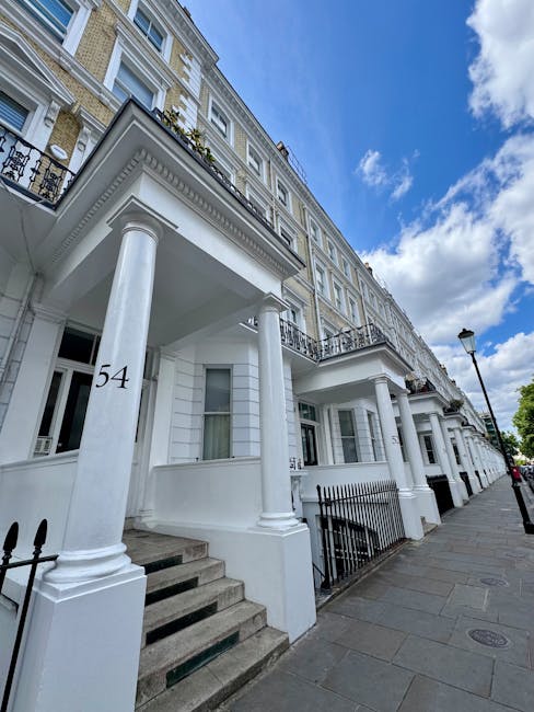 Exterior view of a row of white residential buildings with classical architectural features, including tall columns supporting covered stairways leading to front doors. The buildings have large window