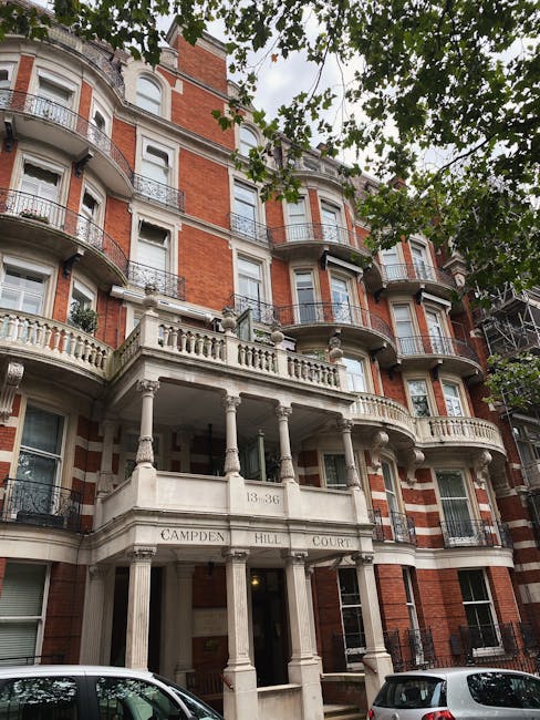 Exterior view of a row of white residential buildings with classical architectural features, including tall columns supporting covered stairways leading to front doors. The buildings have large window